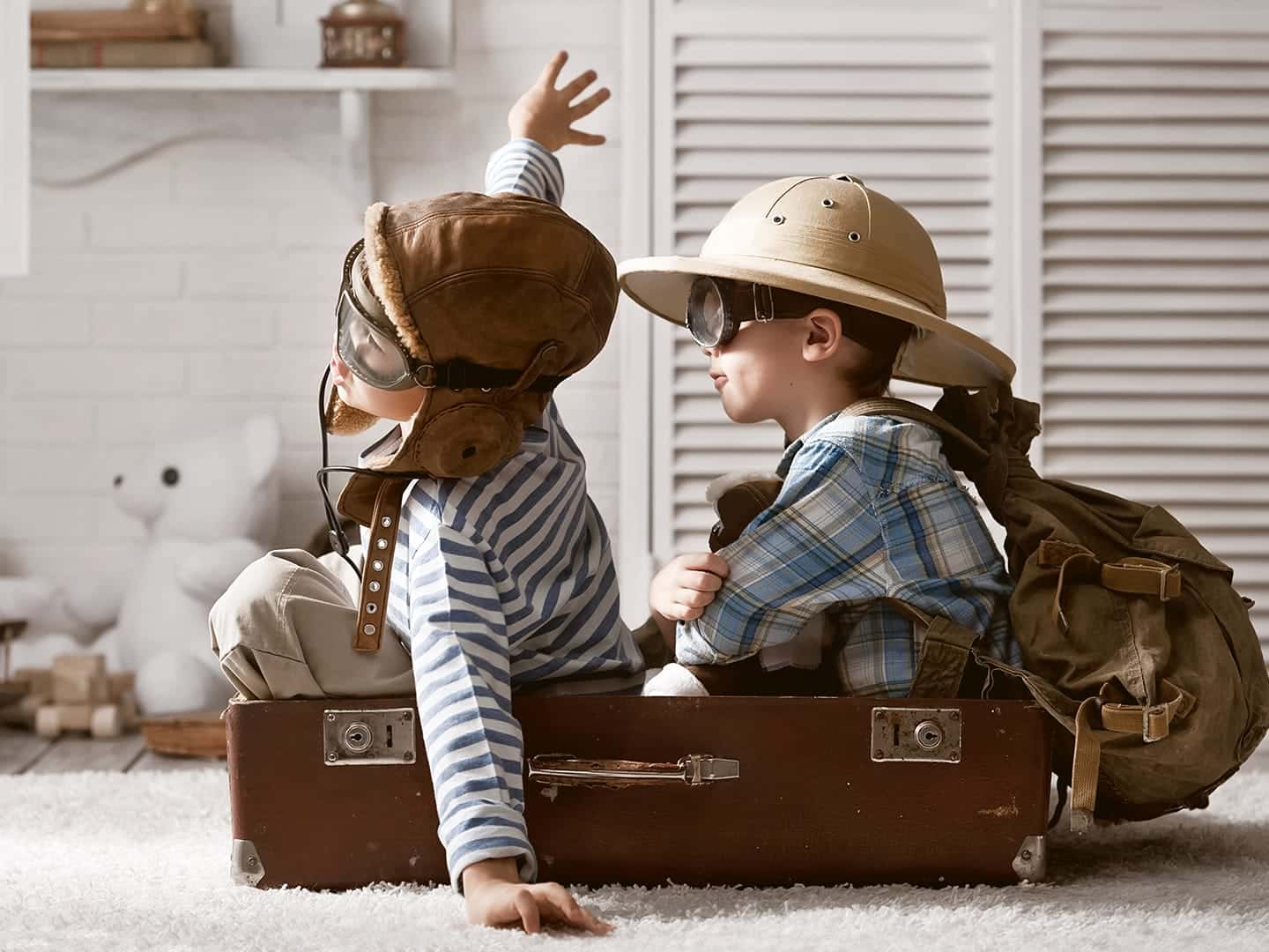 Zwei kleine Kinder sitzen verkleidet als Abenteurer in einem alten Koffer
