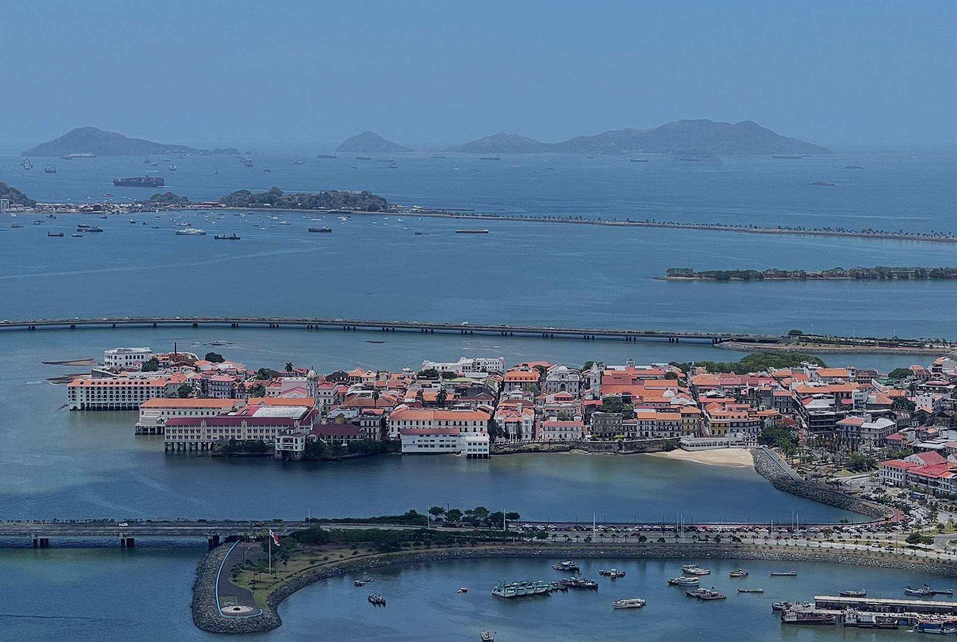 Blick auf Casco Viejo in Panama-Stadt mit bunten Häusern und roten Dächern am Meer, im Hintergrund Boote und Inseln.