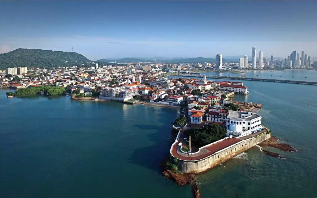 Luftaufnahme des historischen Viertels Casco Viejo in Panama City mit seinen Kolonialbauten und roten Dächern am Wasser, im Hintergrund die moderne Skyline mit Hochhäusern.