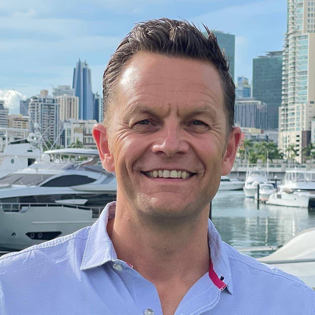 Mann in hellblauem Hemd, Klaus Happ (Geschäftsführender Gesellschafter & Gründer), lächelt in die Kamera, im Hintergrund Yachthafen und moderne Hochhäuser von Panama City.